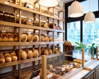 patisserie-Display of various types of freshly baked bread arranged on wooden shelves and inside a glass counter in a bakery shop, creating a warm and inviting atmosphere