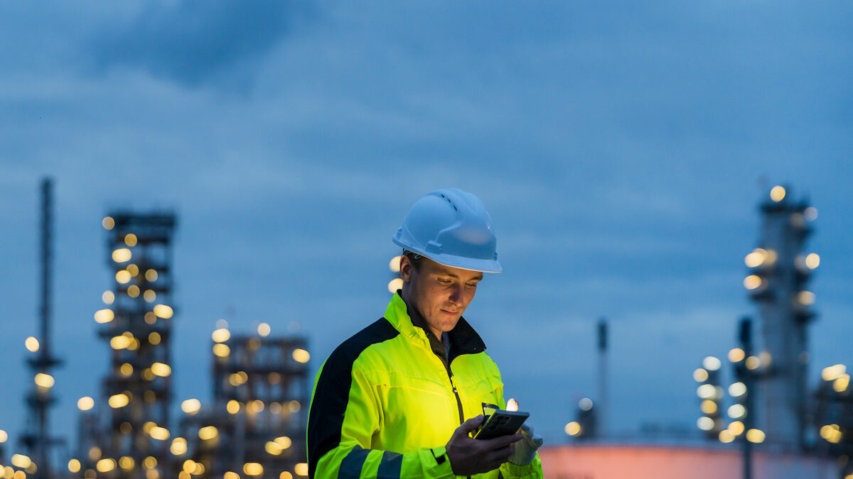 Industrial worker using a smartphone for communication at an oil and gas plant at night.