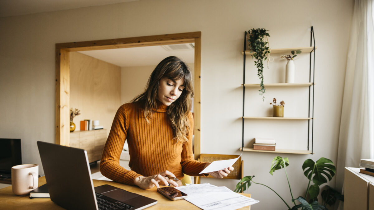 Woman calculating expenses using laptop and smartphone at a modern home office