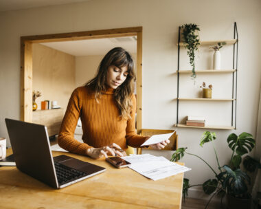 Woman calculating expenses using laptop and smartphone at a modern home office