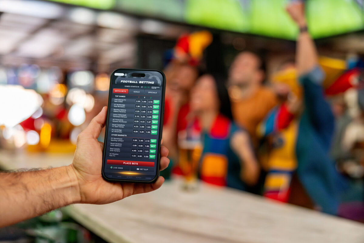 Man holding a cell phone and using a mobile app to bet in sports online - cheerful crowd at the background