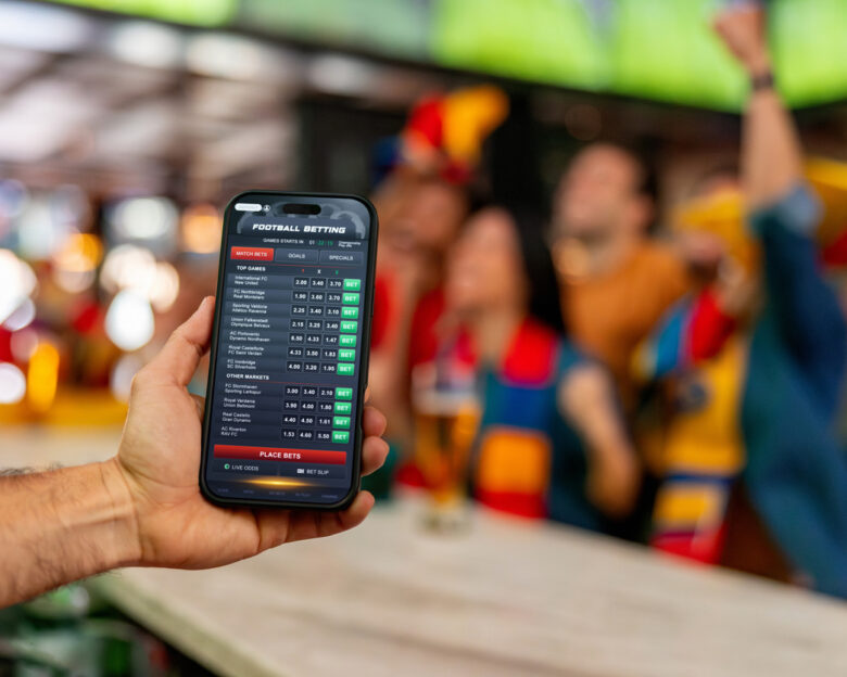 Man holding a cell phone and using a mobile app to bet in sports online - cheerful crowd at the background