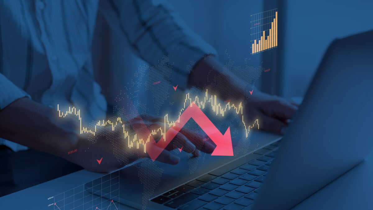 Laptop showing declining gold stock market data with illuminated charts and urban night skyline reflection