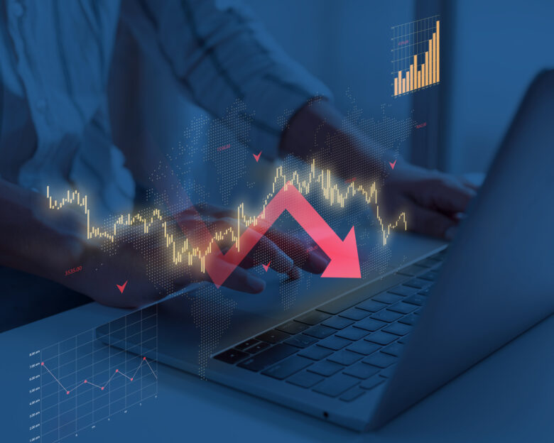 Laptop showing declining gold stock market data with illuminated charts and urban night skyline reflection