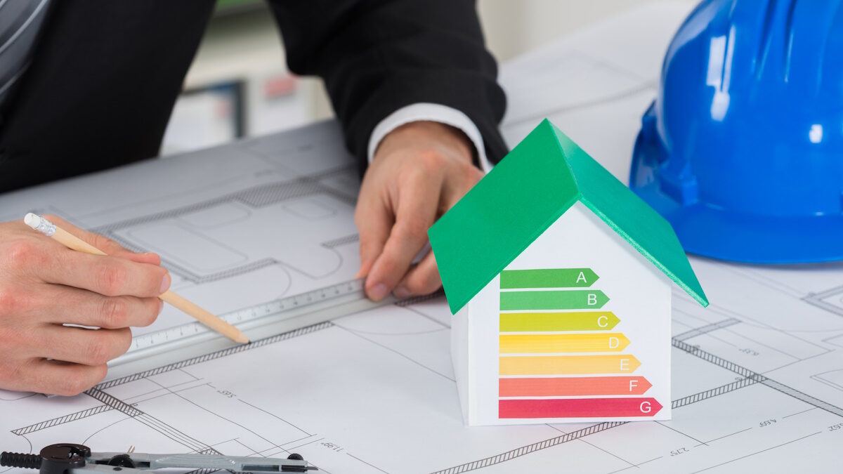 Architect Working On Blue-print Near House Model Showing Energy Efficiency In Office - exoikonomo