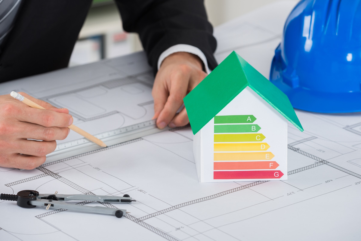 Architect Working On Blue-print Near House Model Showing Energy Efficiency In Office - exoikonomo