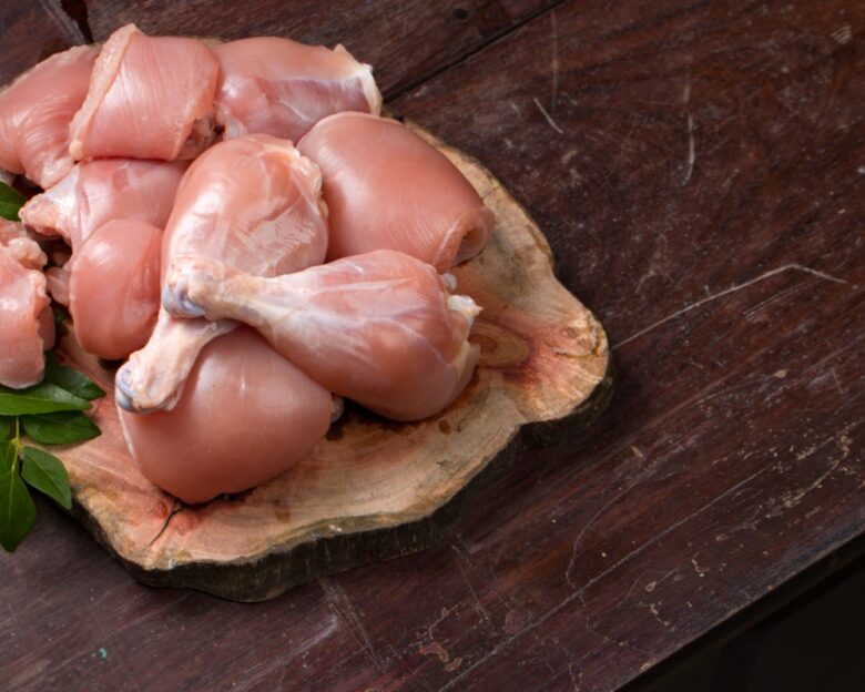 Raw chicken cuts or parts like breast fillet,chicken stripes; Raw chicken cuts or parts like breast fillet,chicken stripes; chicken legs without skin arranged on a sliced wooden log base and garnished with curry leaves and placed on wooden background