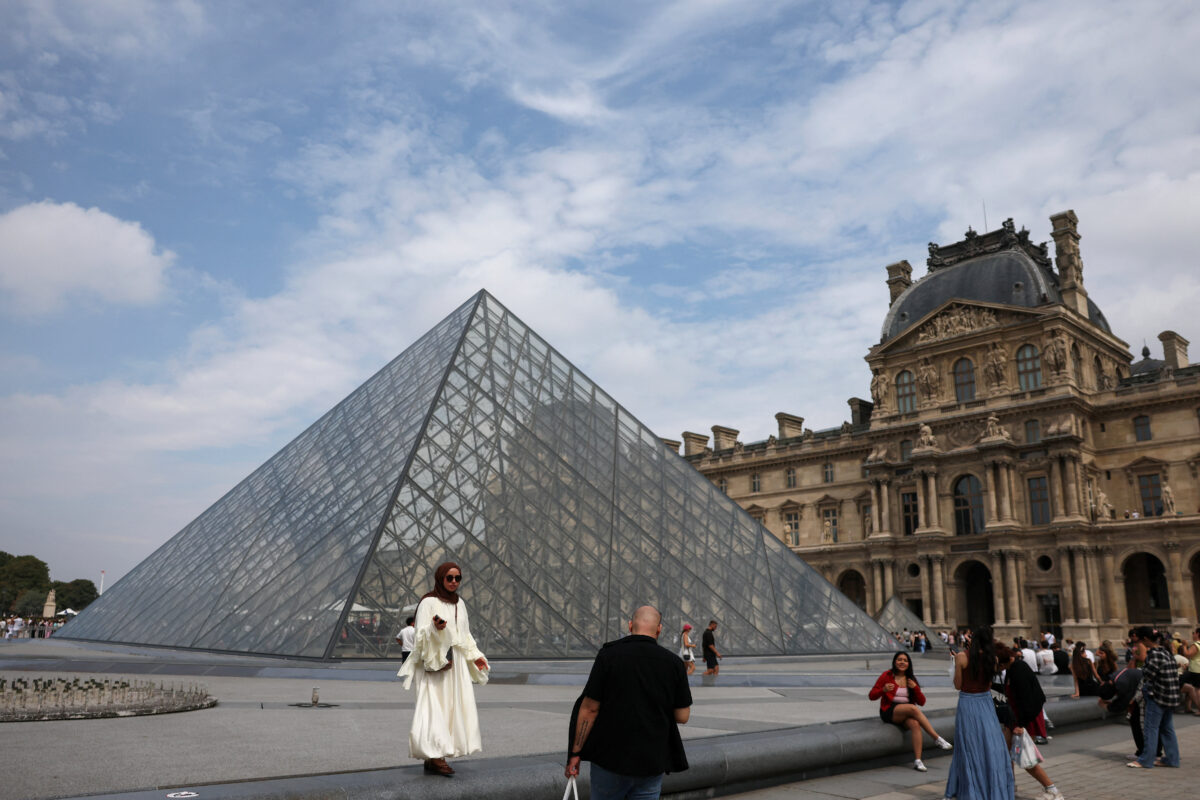 Tourists pose for pictures in front of the glass Pyramid of the Louvre museum on a cloudy summer day in Paris, France, July 17, 2026. REUTERS/Yara Nardi