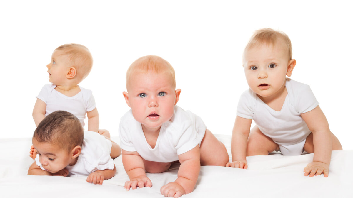 Curious looking group of babies crawl in a row wearing white bodysuit on the white background