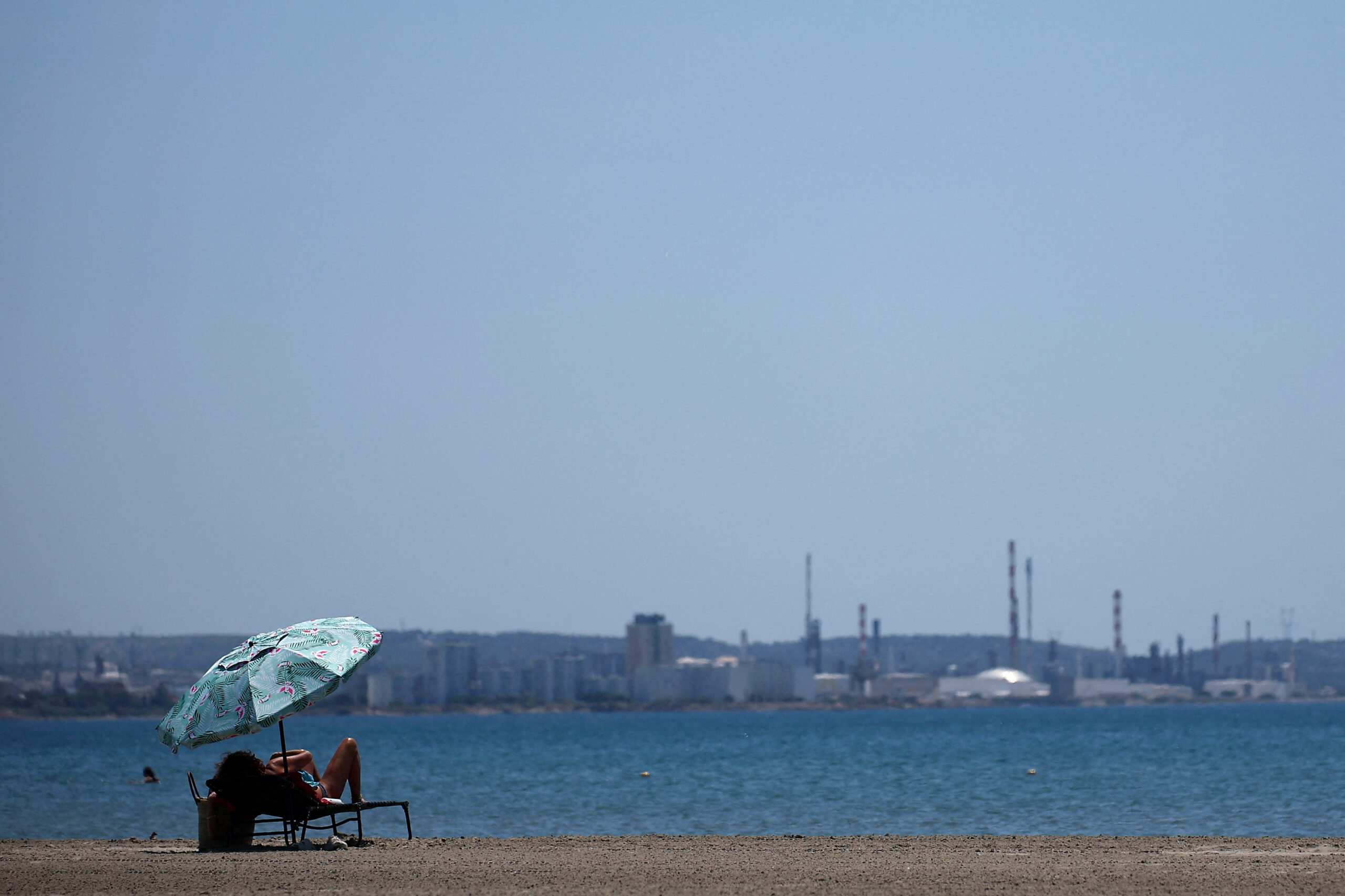 A woman rests under a beach umbrella on Cavaou beach during a heatwave affecting southern France, with the industrial facilities of the Lavera petrochemical complex in the background, in Fos-sur-Mer, France, July 8, 2026. REUTERS/Manon Cruz TPX IMAGES OF THE DAY