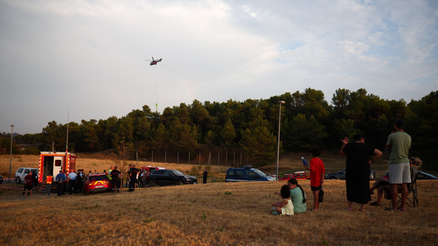 Local residents look on as a firefighting helicopter drops water in Carcassonne, Aude department, amid worsening drought conditions following a heatwave and water shortages across much of France, August 2, 2026.