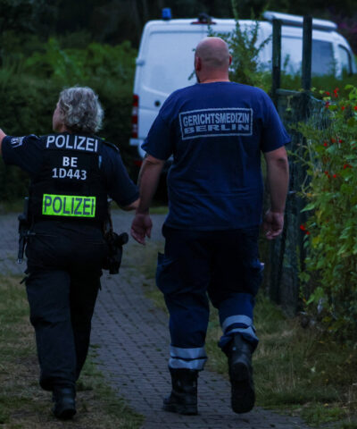 Forensic medicine expert walks with a police officer at an allotment garden complex in the Berlin suburb of Spandau after a known Islamist, suspected of ramming a minivan into a crowd near Berlin's annual Christopher Street Day Pride parade on Saturday evening, was shot and killed in a police operation, in Berlin, Germany, July 26, 2026. REUTERS/Christian Mang