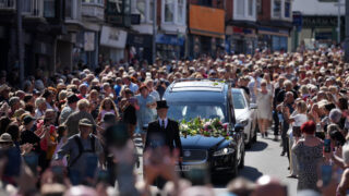 Fans of singer Bonnie Tyler line the streets as her coffin is transported in a hearse back to her former home ahead of her funeral, in Mumbles, Wales, Saturday, Aug. 15, 2026. The Total Eclipse Of The Heart musician, whose real name was Gaynor Hopkins, died in hospital in Portugal on July 8 at the age of 75.