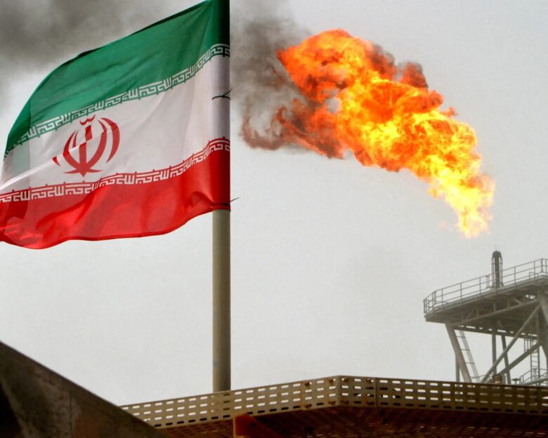 FILE PHOTO: A gas flare on an oil production platform is seen alongside an Iranian flag in the Gulf July 25, 2005.