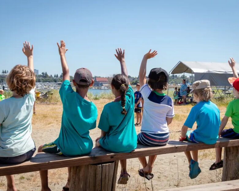 Students holding their hands up to volunter or ask questions of their teacher at an outdoor nature class. Jetty Island Washington.