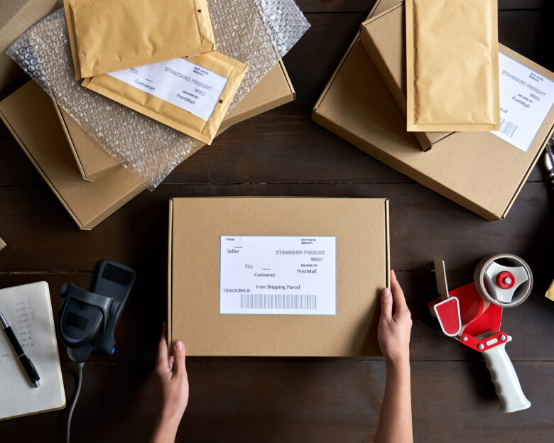 Above table top view of female warehouse worker or seller packing ecommerce shipping order box for dispatching, preparing post courier delivery package, dropshipping shipment service concept.