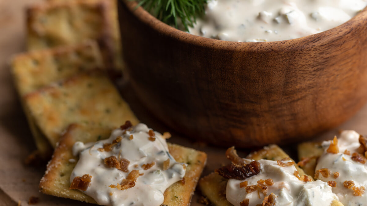 Creamy jalapeno dip with bacon pieces on crackers. Closeup view
