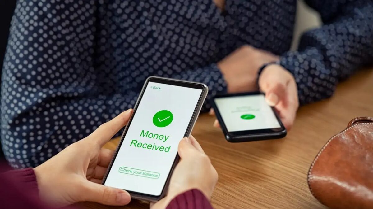 Close up of woman hands holding mobile phone with application to receive money. People holding smart phone and making cashless payment transaction in a shop. Close up of smartphone screen displaying payment sent with money received message.