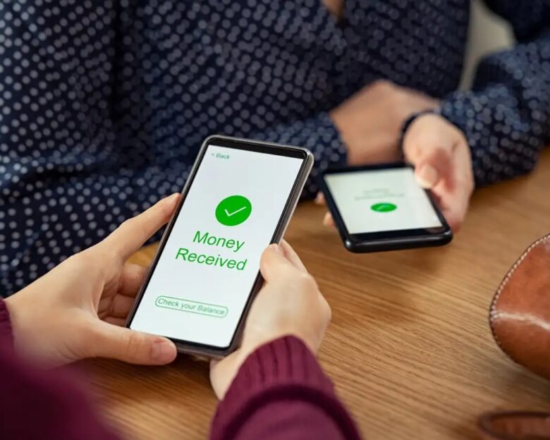 Close up of woman hands holding mobile phone with application to receive money. People holding smart phone and making cashless payment transaction in a shop. Close up of smartphone screen displaying payment sent with money received message.
