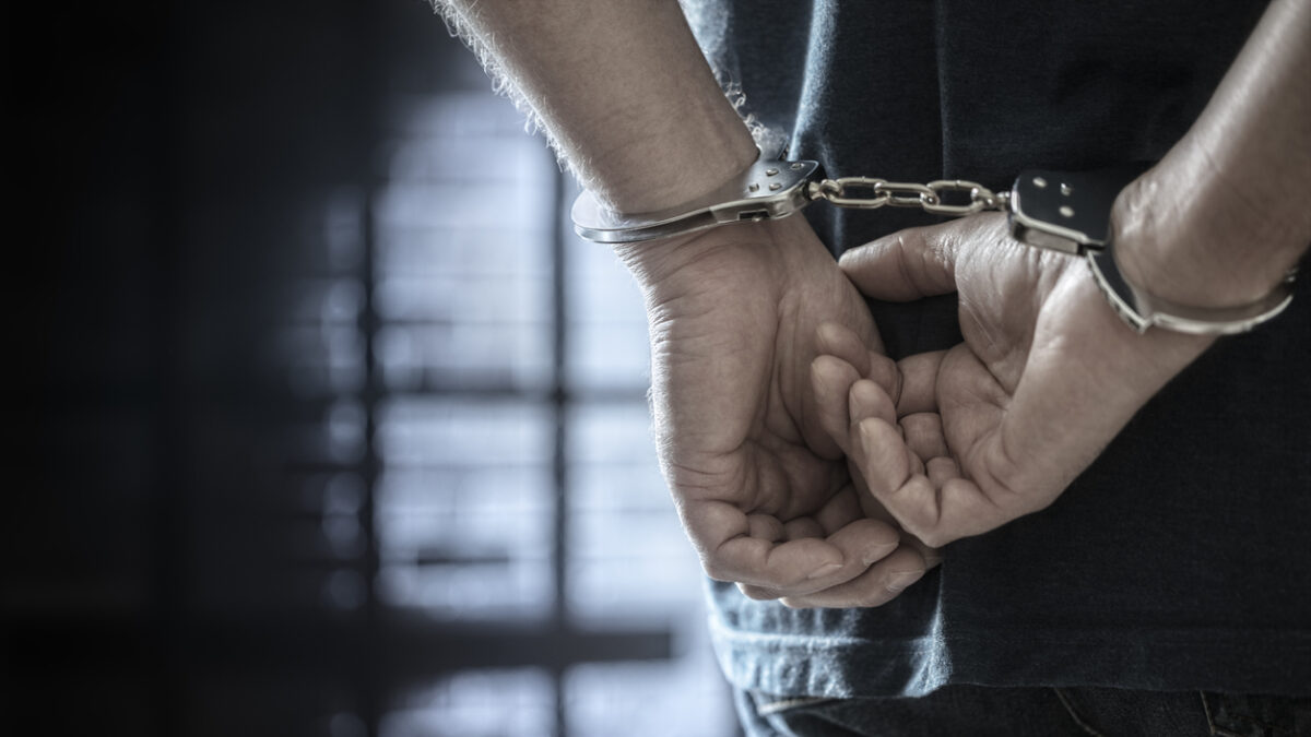 Arrested man in handcuffs with handcuffed hands behind back in prison