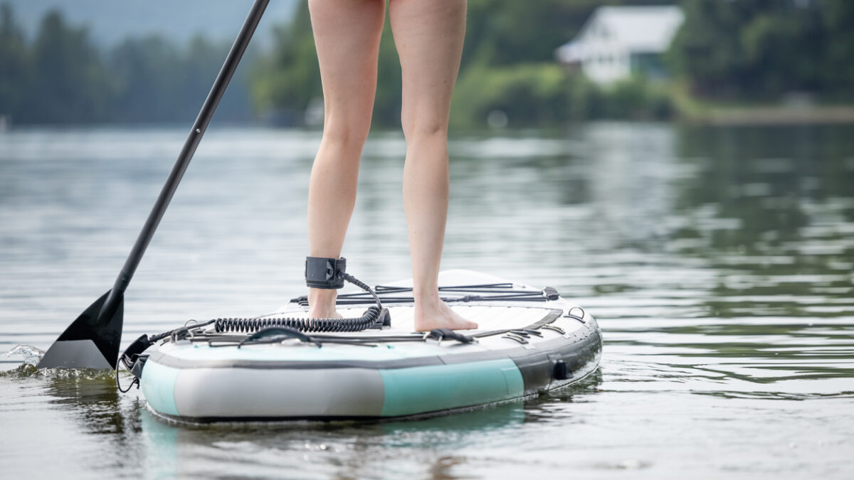 Woman Stand up paddle-boarding on quiet lake during a warm sunny summer vacation day. Active woman, close-up of water surface, legs and board.