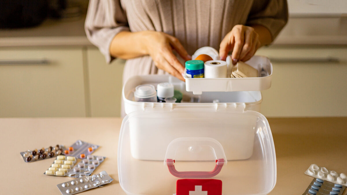 Closeup female hand neatly placing medicament at domestic first aid kit top view. Storage organization in transparent plastic box drug, pill, syringe, bandage. Fast health help safety emergency supply