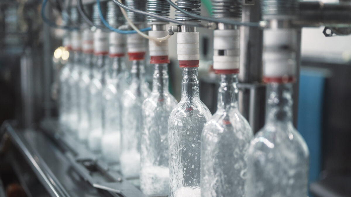 Equipment pours vodka into glass bottles on automated production line with conveyor in workshop of modern plant close view