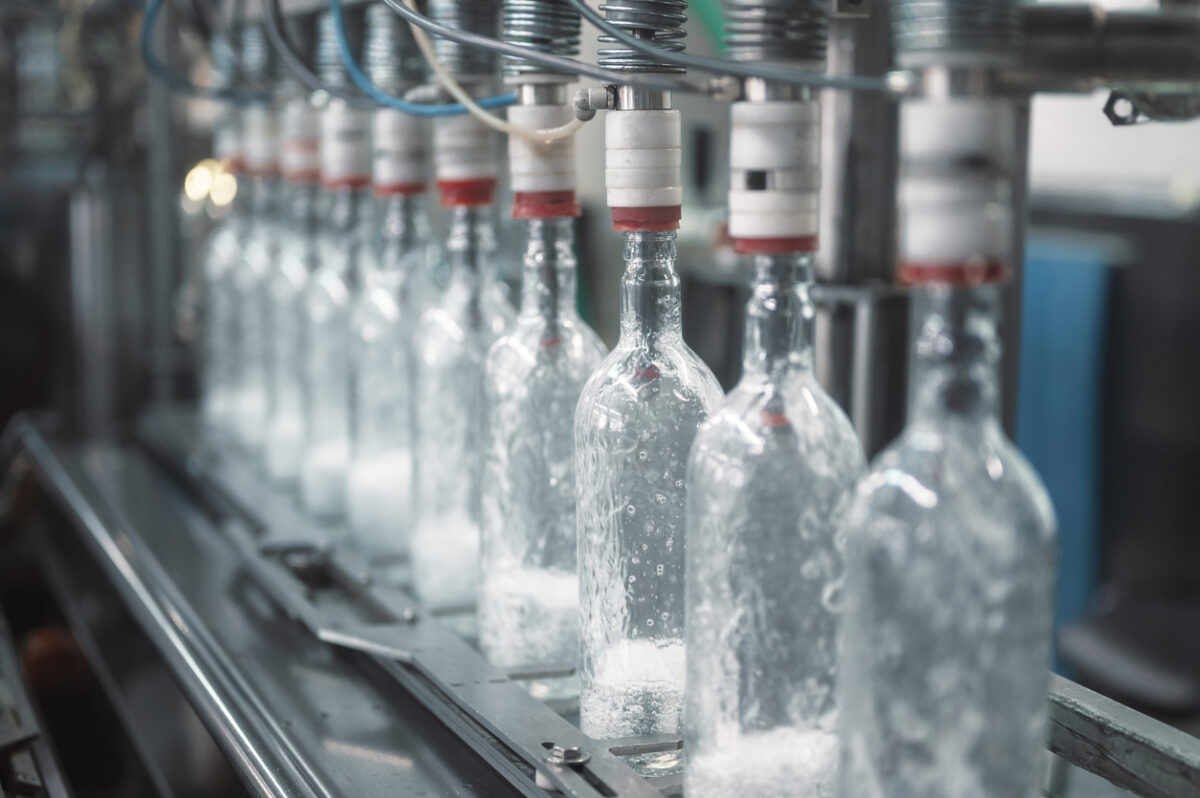 Equipment pours vodka into glass bottles on automated production line with conveyor in workshop of modern plant close view