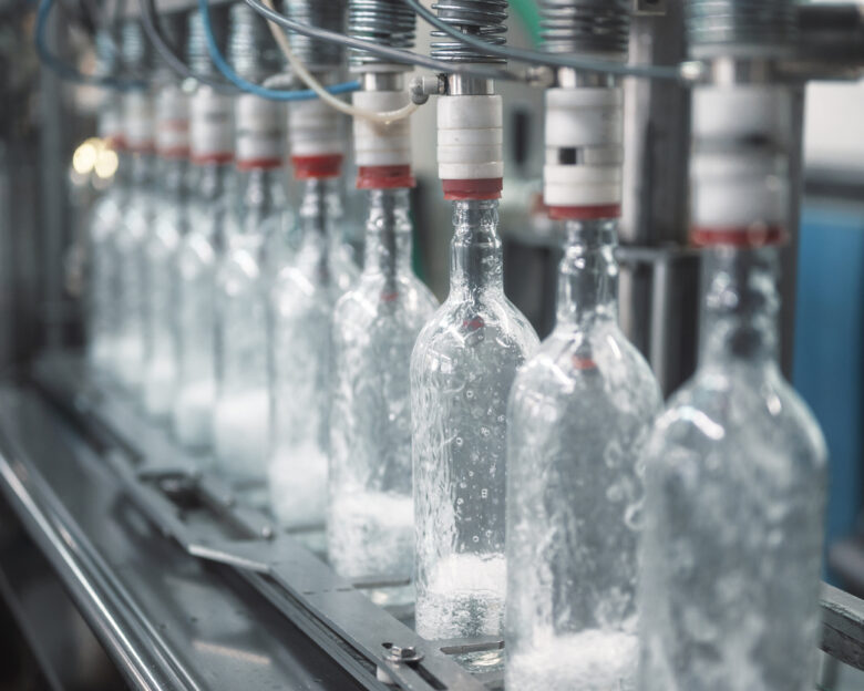 Equipment pours vodka into glass bottles on automated production line with conveyor in workshop of modern plant close view