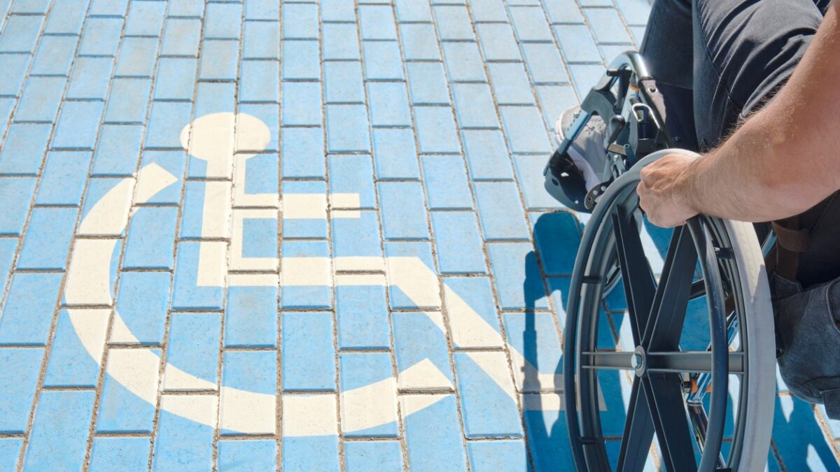 unrecognizable handicapped man in a wheelchair passing over blue and white handicapped sign painted on the floor