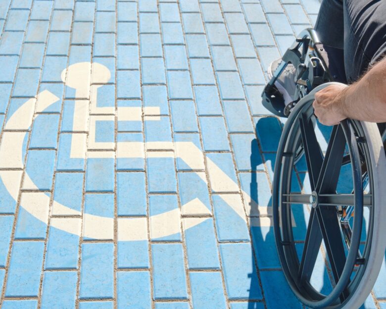 unrecognizable handicapped man in a wheelchair passing over blue and white handicapped sign painted on the floor