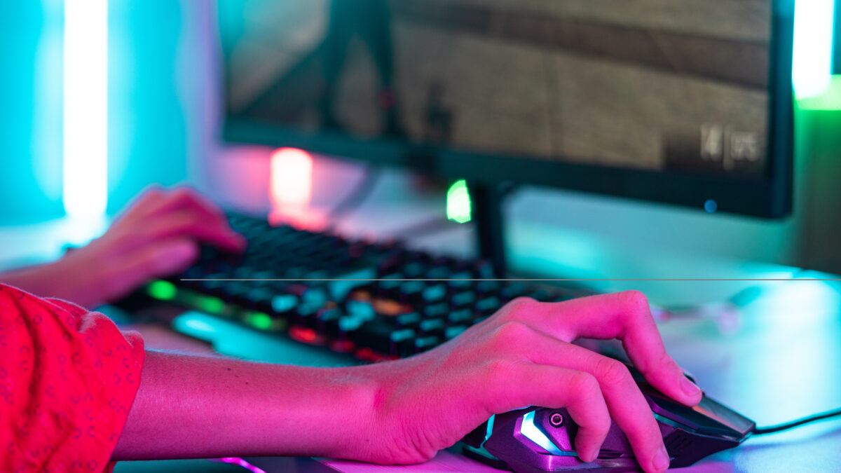 Close up shot of teenager kid hands using mouse while playing video game at neon light background - concept of entertainment, hobbies and technology
