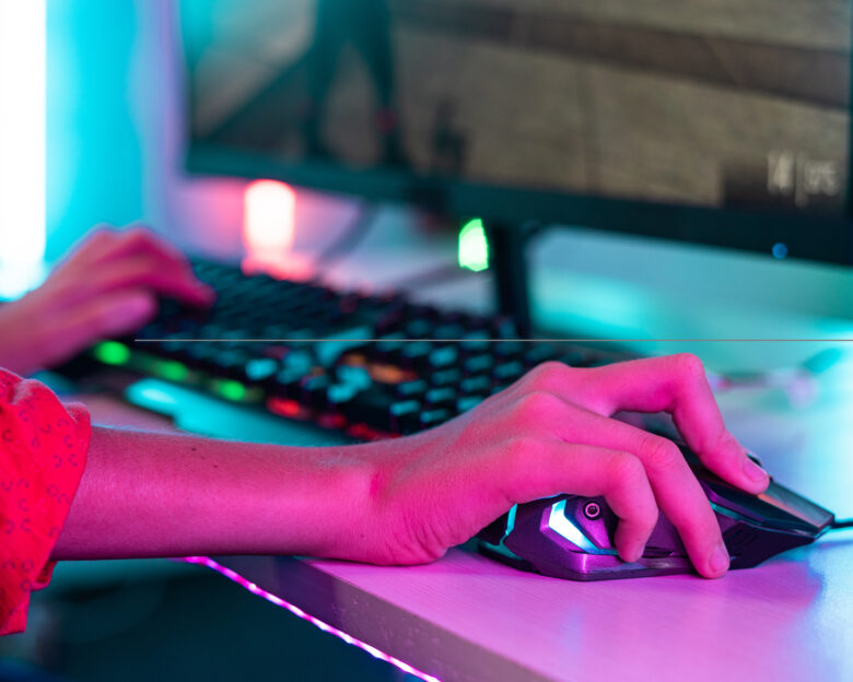 Close up shot of teenager kid hands using mouse while playing video game at neon light background - concept of entertainment, hobbies and technology