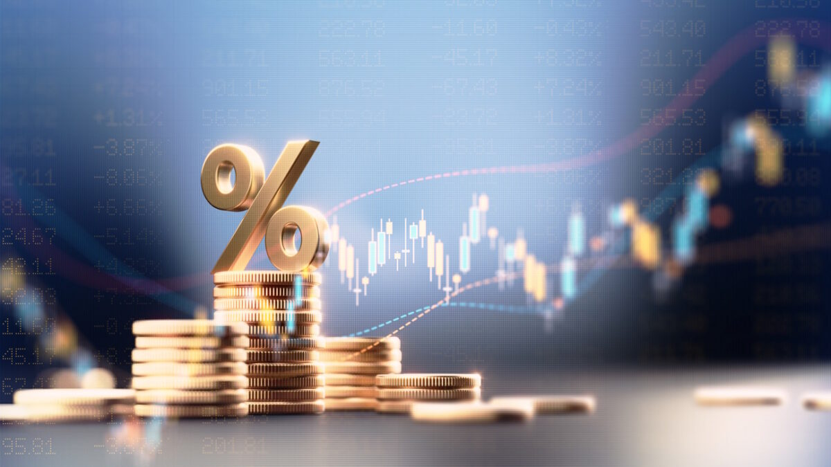 Percentage sign on top of coin stacks before blue financial graph. Horizontal composition with copy space. Business and finance concept.