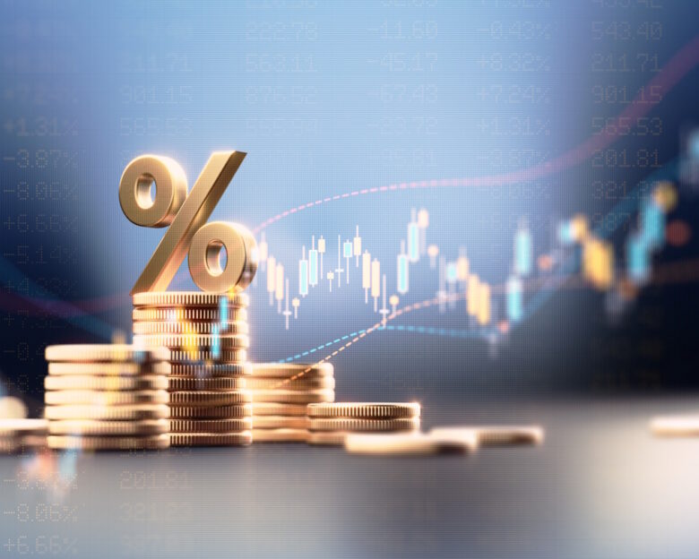 Percentage sign on top of coin stacks before blue financial graph. Horizontal composition with copy space. Business and finance concept.