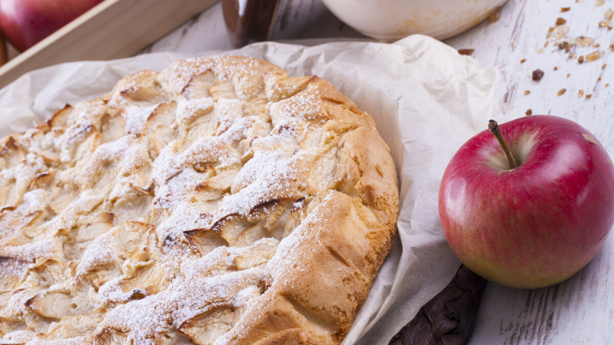 Sweet dessert rounded apple cake on the cooking paper and brown wooden mat