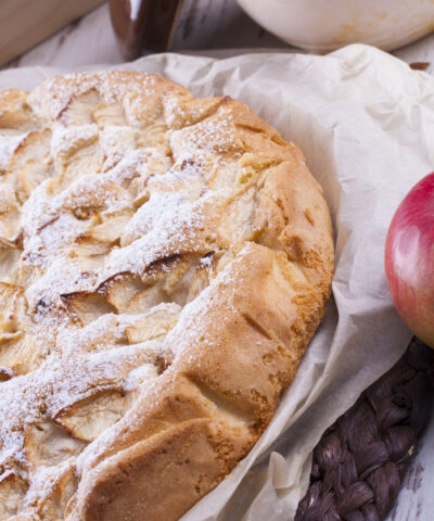 Sweet dessert rounded apple cake on the cooking paper and brown wooden mat