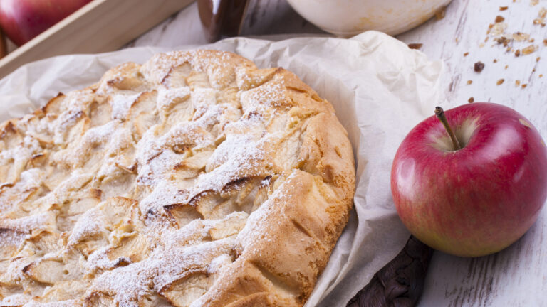 Sweet dessert rounded apple cake on the cooking paper and brown wooden mat