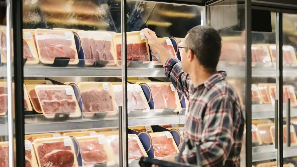 Male customer with a shopping basket taking meat from a fridge at local supermarket