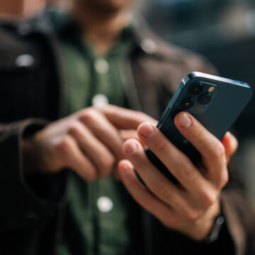Close-up hands of unrecognizable man holding and using smartphone standing on city street, browsing internet, checking social media, using mobile application. Concept of modern communication.