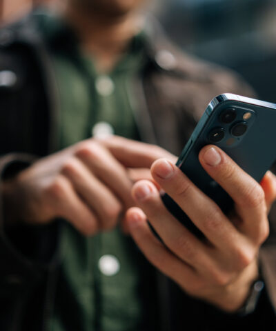 Close-up hands of unrecognizable man holding and using smartphone standing on city street, browsing internet, checking social media, using mobile application. Concept of modern communication.