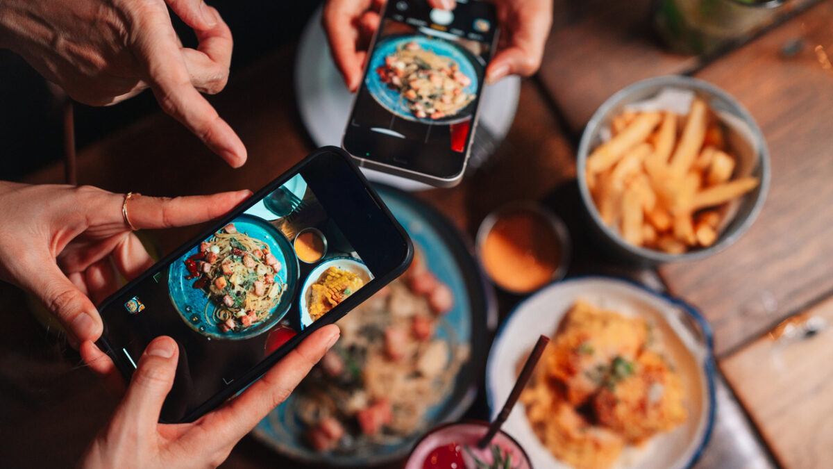 Close-up shot of group of friends using their smartphones to take pictures of the food on the table, living the camera eats first moment as they capture the perfect shot before digging into their delicious meal and enjoying the experience together