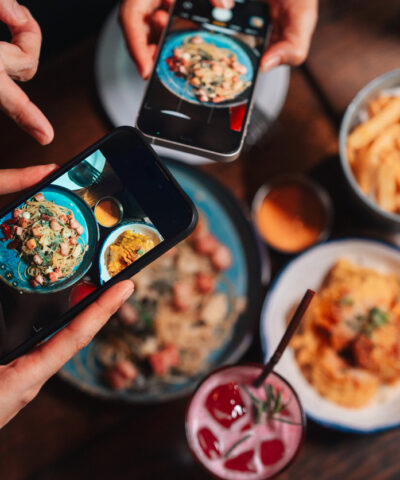 Close-up shot of group of friends using their smartphones to take pictures of the food on the table, living the camera eats first moment as they capture the perfect shot before digging into their delicious meal and enjoying the experience together