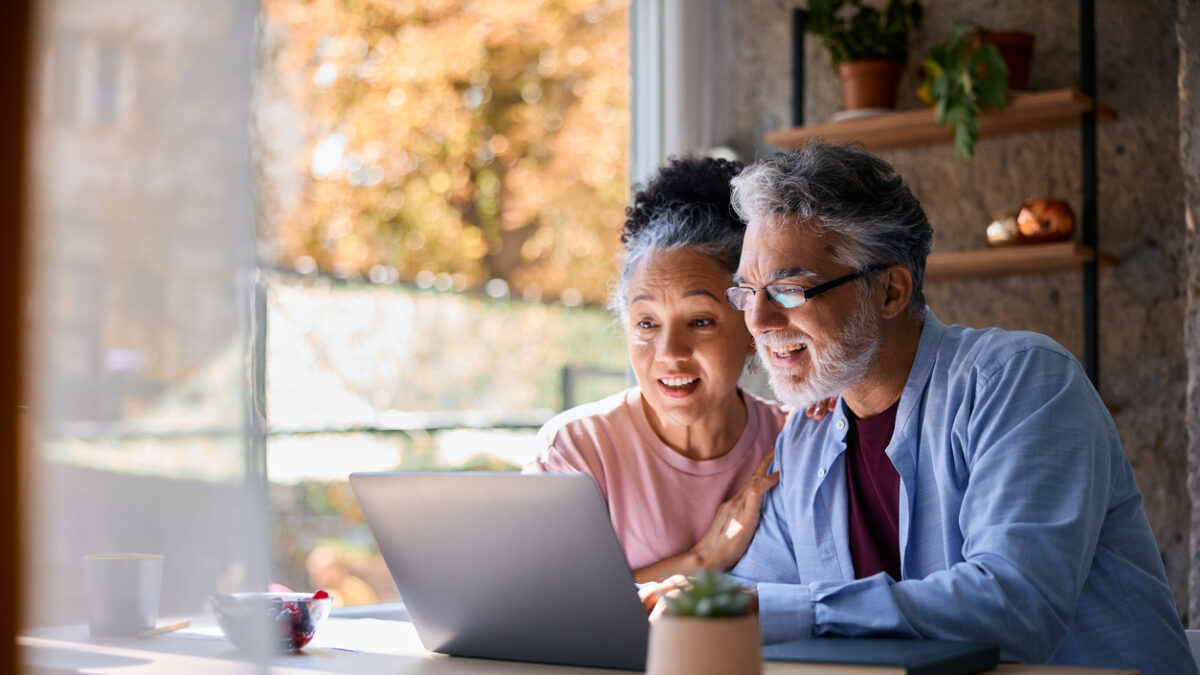Surprised senior couple sitting together at home, gazing at their laptop screen, sharing in the joy of good news and experiencing a moment of happiness and connection