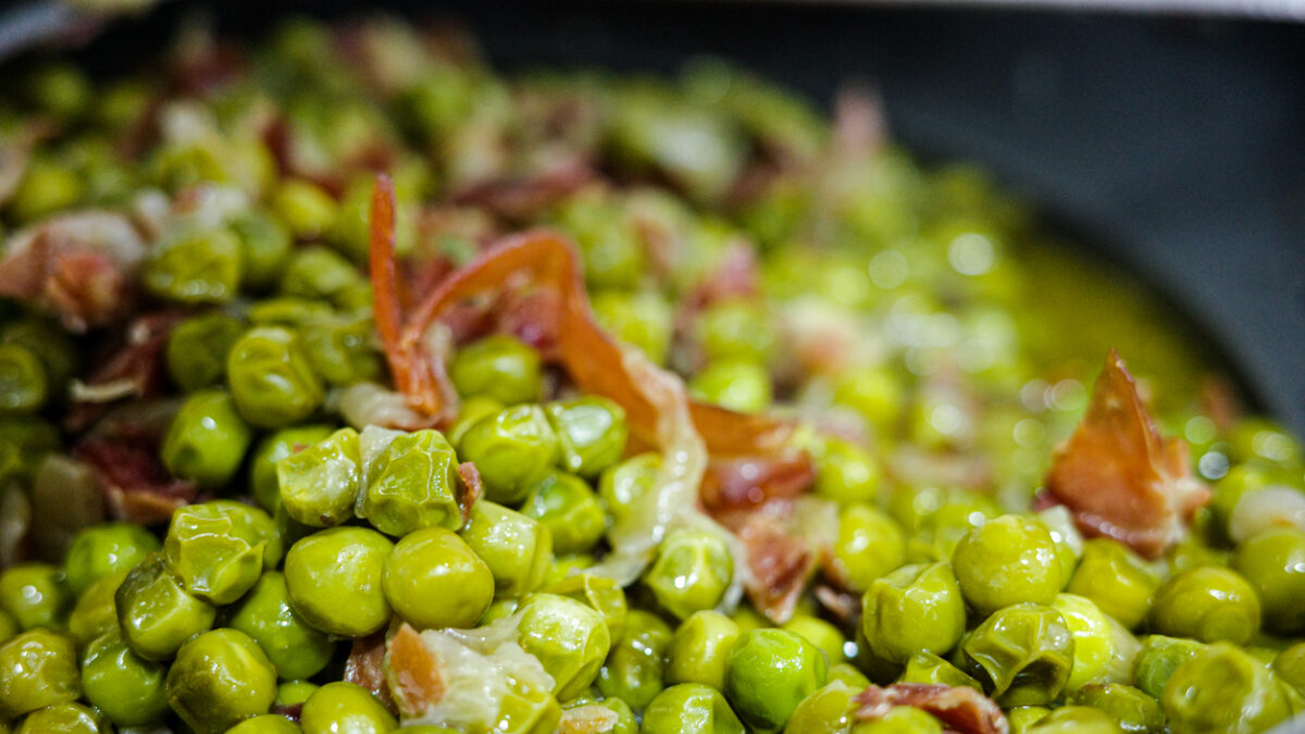 Close-up of green peas cooked with cured ham in olive oil. Typical homemade Spanish recipe, healthy Mediterranean cuisine.