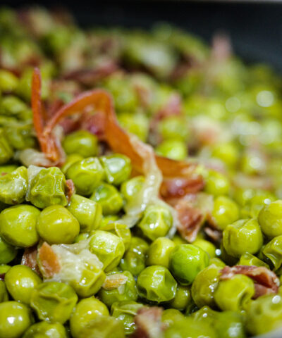 Close-up of green peas cooked with cured ham in olive oil. Typical homemade Spanish recipe, healthy Mediterranean cuisine.