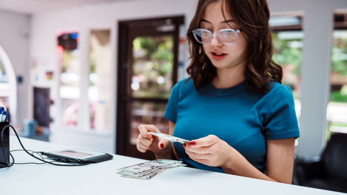 A teenage girl of Hispanic descent places US currency on the bank counter when making a deposit into her account at a credit union.