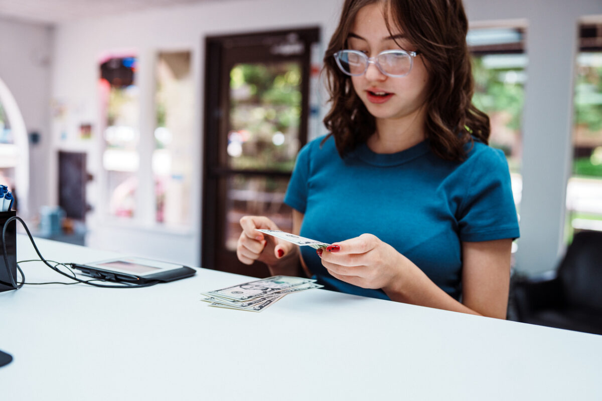A teenage girl of Hispanic descent places US currency on the bank counter when making a deposit into her account at a credit union.