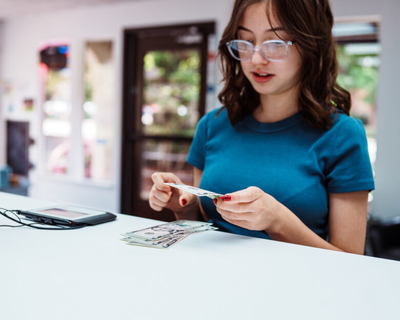 A teenage girl of Hispanic descent places US currency on the bank counter when making a deposit into her account at a credit union.