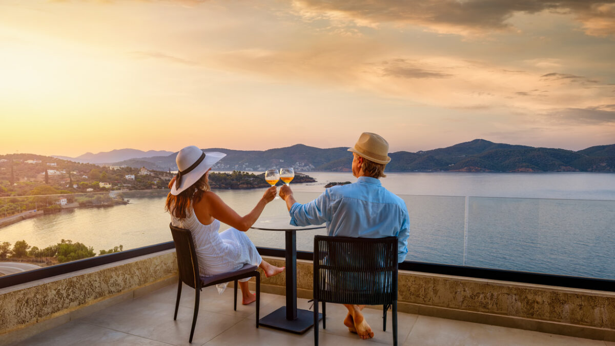 A elegant holiday couple enjoys the beautiful summer sunset in the mediterranean sea with a glass of wine, romantic honeymoon vacation concept